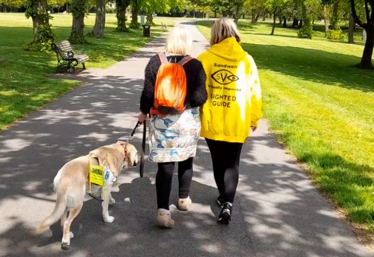 Sighted guide walks with visually impaired woman and guide dog in Dartmouth Park