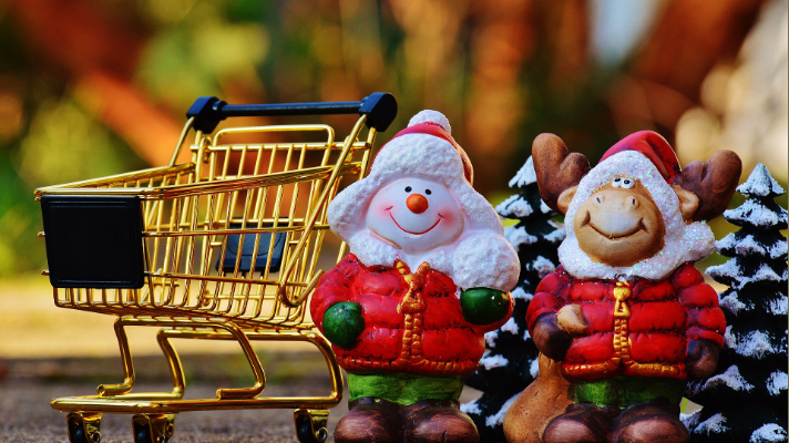 A model snowman and reindeer sit by a Christmas tree with a shopping trolley