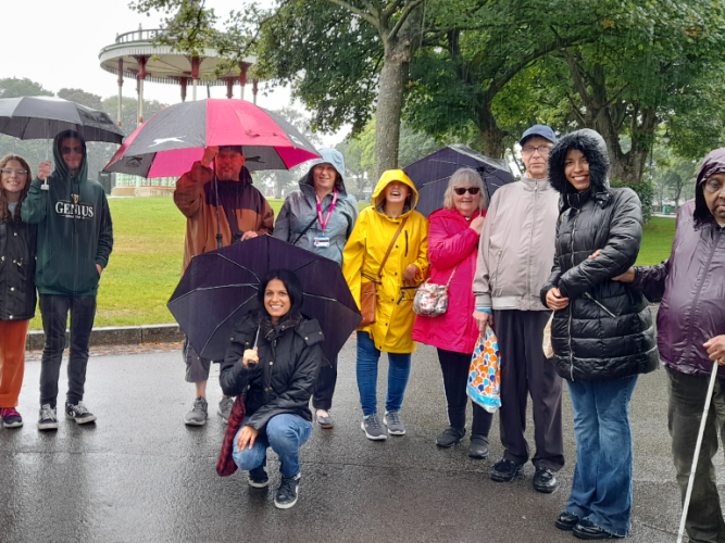 A group of SVI members and volunteers standing smiling under umbrellas on a park walk