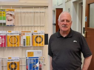 Nigel Self, SVI Volunteers Coordinator by the leaflet rack in the foyer of the SVI offices