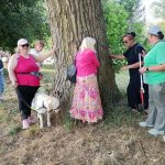 A group, plus a guide dog, stand around the tree, feel the rough bark of a tree